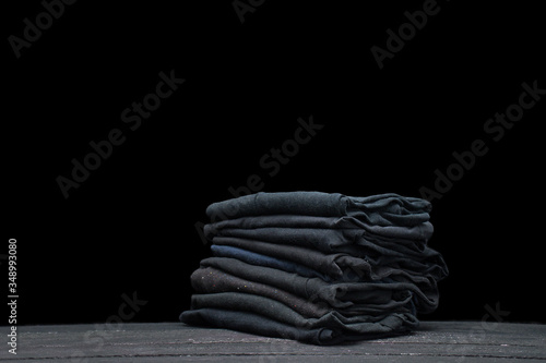 Pile of black T-shirts isolated on black background, a Black Friday sale concept, with copyspace for text