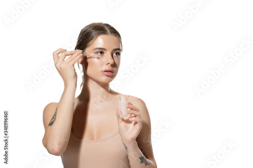 Portrait of beautiful young woman with essential oil pouring over white background. Concept of cosmetics, makeup, natural and eco treatment, skin care. Shiny and healthy skin, fashion, healthcare.