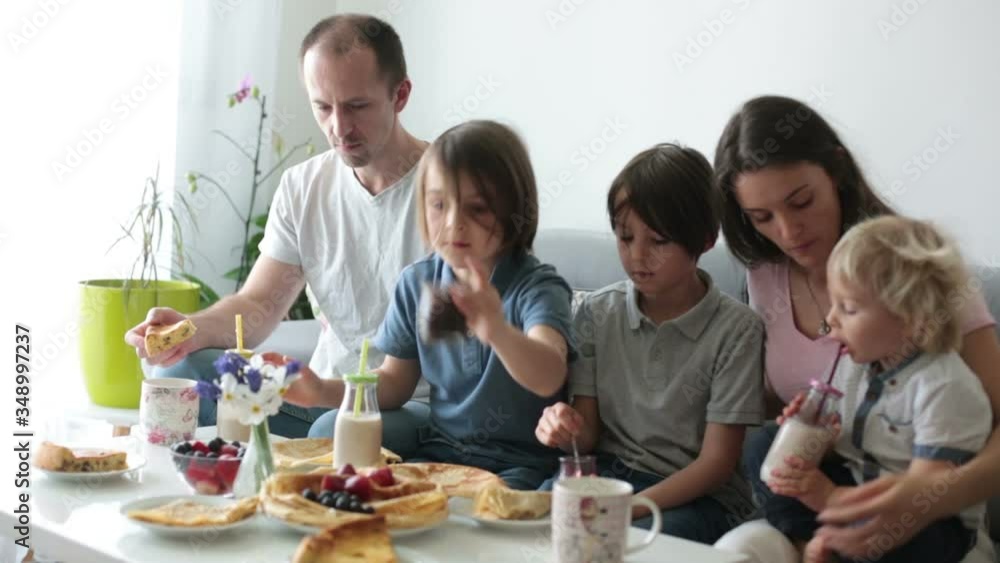 Happy family, having pancakes for breakfast, eating in living room, talking and laughing, cozy home Happy family, having pancakes for breakfast, eating in living room, talking and laughing, cozy home