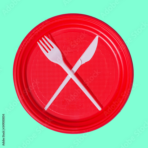 Disposable plastic tableware, red plate, white knife and spoon on mint background photo