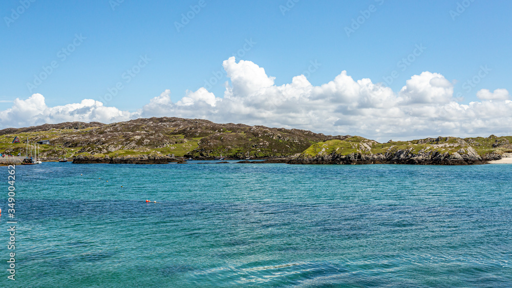 Rocky hills along the coast of Inishbofin Island, calm turquoise water, sunny spring day with blue sky and white clouds in County Galway, Ireland