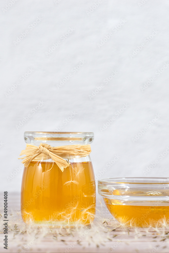 Dandelion jam, honey, jelly in a glass jar on a wooden table, white background with fresh flowers, dandelion airy seed heads, seeds, blow balls. Medicine, healthy food, health benefits from nature Dandelion jam, honey, jelly in a glass jar on a wooden table, white background with fresh flowers, dandelion airy seed heads, seeds, blow balls. Medicine, healthy food, health benefits from nature