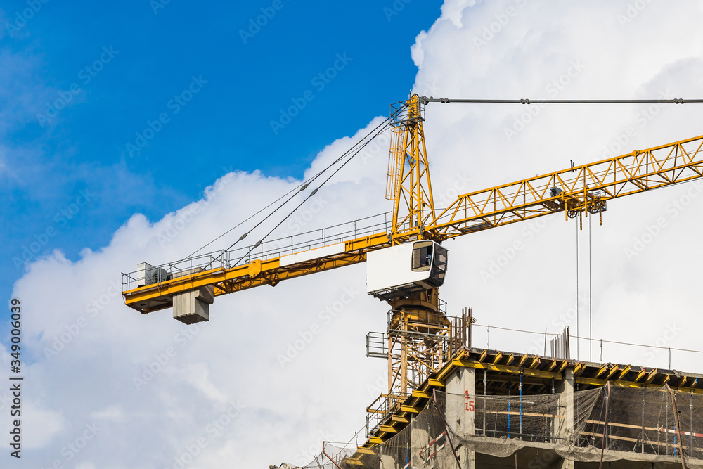 One amber high-rise crane against a house and sky during the construction phase. Industry concept for low-income young families. Mortgage, business, real estate loan. Copy space.