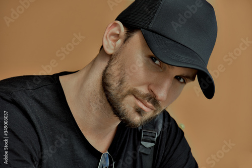 Young handsome attractive serious sexy male police guard with a beard and mustache. a brunette man in a black casual suit and a cap with a baseball cap looks piercingly passionately at the camera 