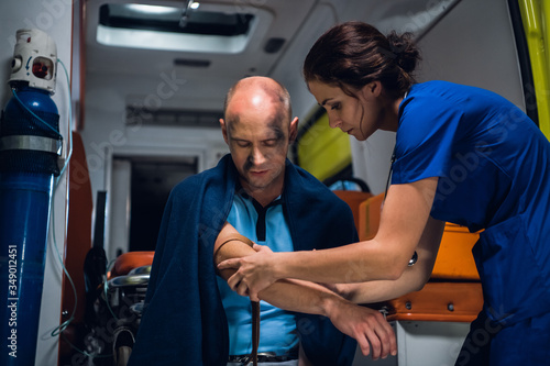 A woman in a blue uniform wraps a tourniquet around a hand of an injured man