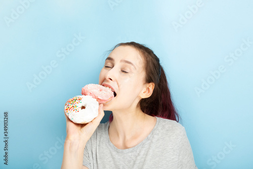 Young girl holds two donuts in her hand and bites one from enjoying closing her eyes  blue background