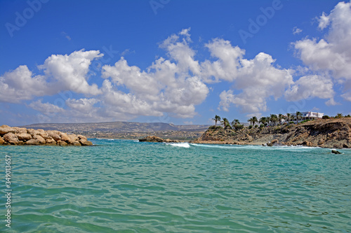 Seascape, view of the rocky coast with palm trees growing on it. On a bright sunny day with blue sky and clouds