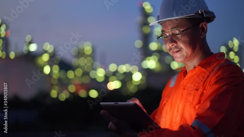 Asian engineer man using digital tablet working late night shift at petroleum oil refinery.