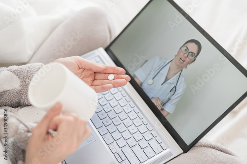 Unrecognizable woman drinks pills as prescribed by a doctor at an online consultation. Female doctor talking to a sick patient on a webcam. Girl with the flu on sick leave.
