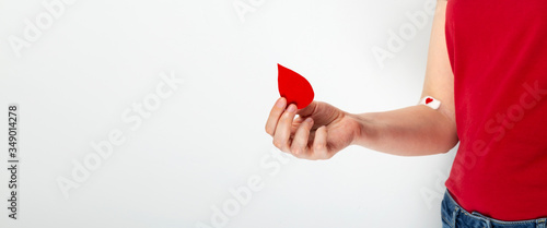 Blood donorship. Young girl in red T-shirt holds drop in her hand, the second hand taped with patch   with red heart after giving blood on gray background. Copy space photo