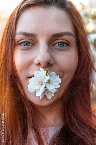 Portrait of young beautiful girl with green eyes with a branch of apple tree in the lips in the garden