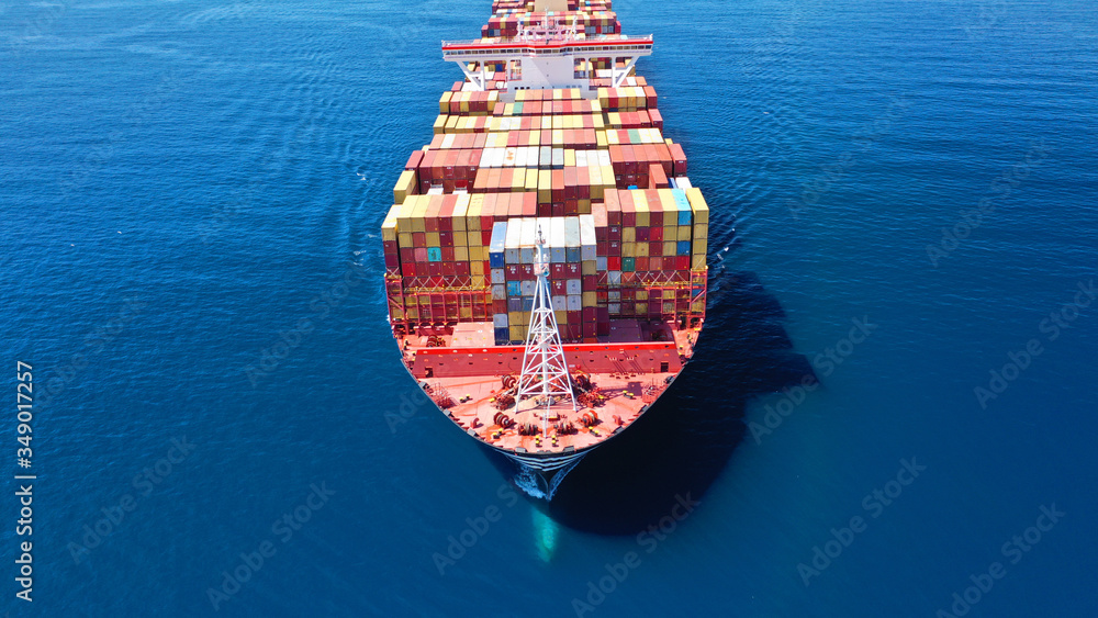 Fototapeta premium Aerial drone photo of huge container cargo Ship carrying load in truck-size colourful containers cruising deep blue open ocean Mediterranean sea 