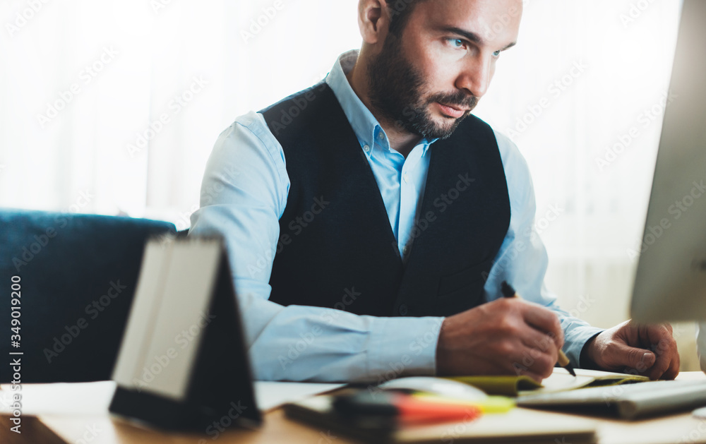 Bearded businessman writes in notebook at home workplace. Manager working at office. Finance consultant thinking looking in monitor computer, online internet work process concept, social distance Bearded businessman writes in notebook at home workplace. Manager working at office. Finance consultant thinking looking in monitor computer, online internet work process concept, social distance