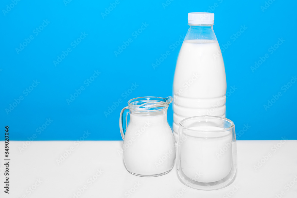 on a white table stands a bottle and glasses and a decanter with milk on a blue background. High calcium content. Healthy drink. on a white table stands a bottle and glasses and a decanter with milk on a blue background. High calcium content. Healthy drink.