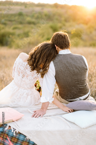 a young couple of newlyweds sitting in comfort on a pillows huggling each other and look out into nature - fields and sunset. The concept of wedding photo