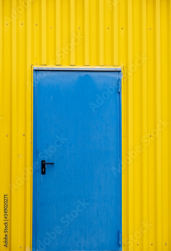Blue close metal door on a yellow wall.