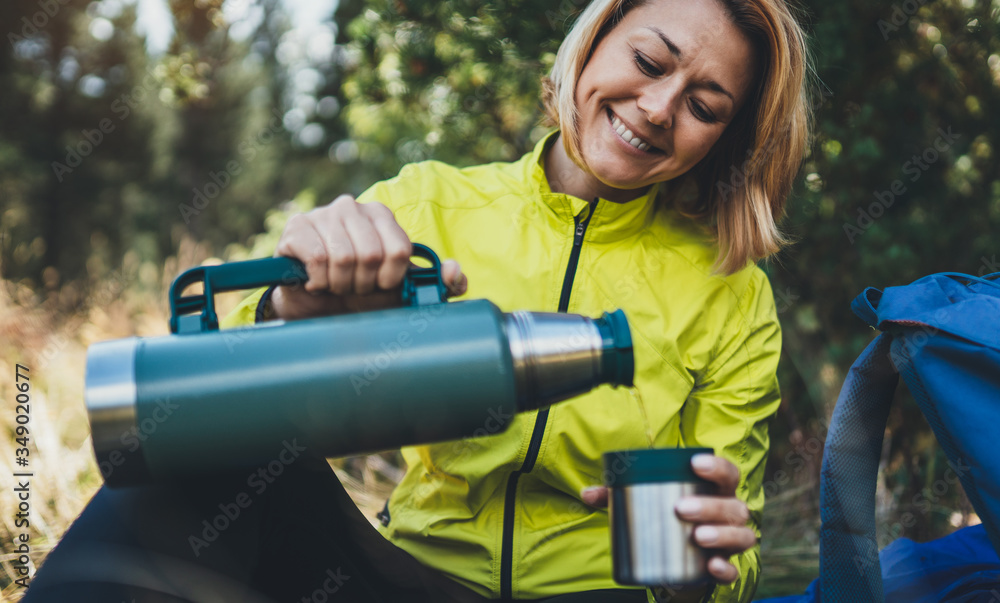 Girl smiles drink coffee from thermos on nature after training, woman hold hand mug of warm tea outdoors, hiker enjoys breakfast rest in green forest. Tourist relax while traveling Girl smiles drink coffee from thermos on nature after training, woman hold hand mug of warm tea outdoors, hiker enjoys breakfast rest in green forest. Tourist relax while traveling