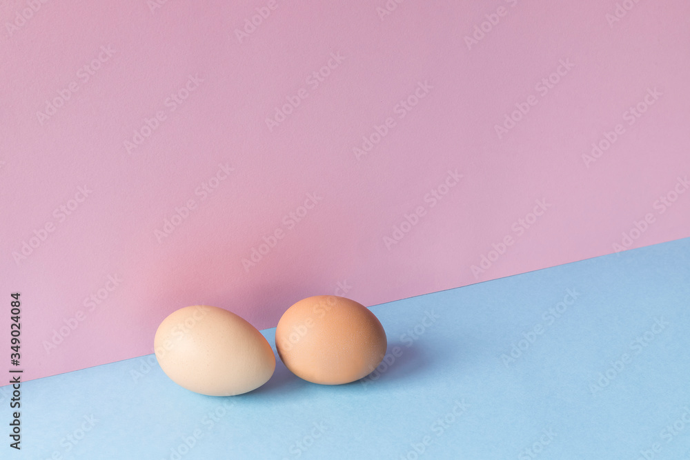 Two brown eggs on a light blue and pink background