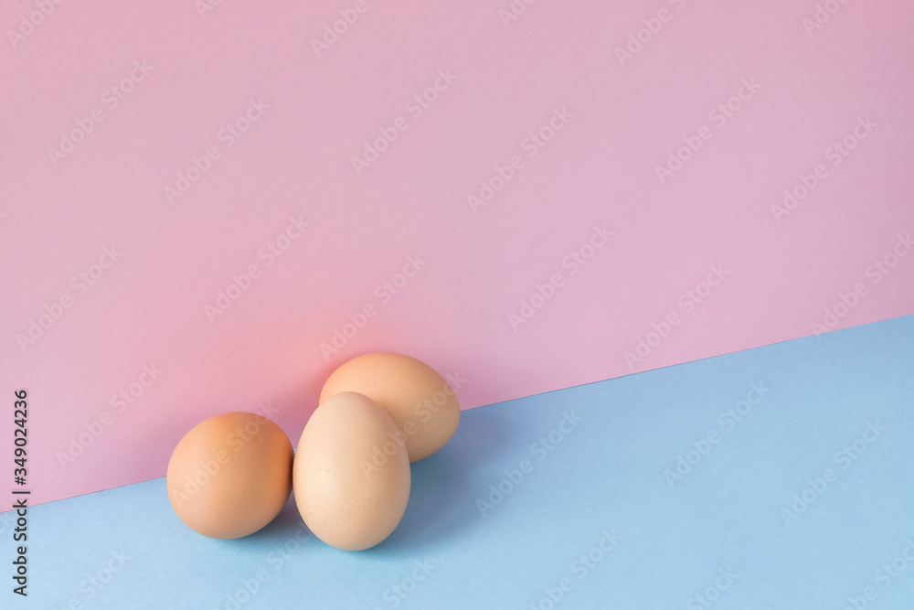 Fototapeta premium Three brown eggs on a light blue and pink background