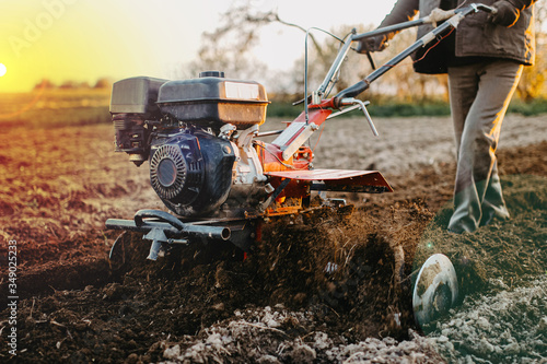 male farmer with a walk-behind tractor cultivates the land with a plow at sunset.