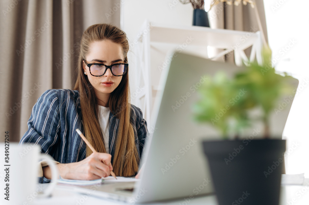 Online education. Young attractive girl with glasses is learning online using a laptop at home Online education. Young attractive girl with glasses is learning online using a laptop at home