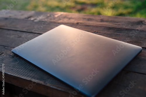 Single laptop computer on a wooden table. Laptop lying on a wooden table behind which is sunset. Laptop. Free space for your text.