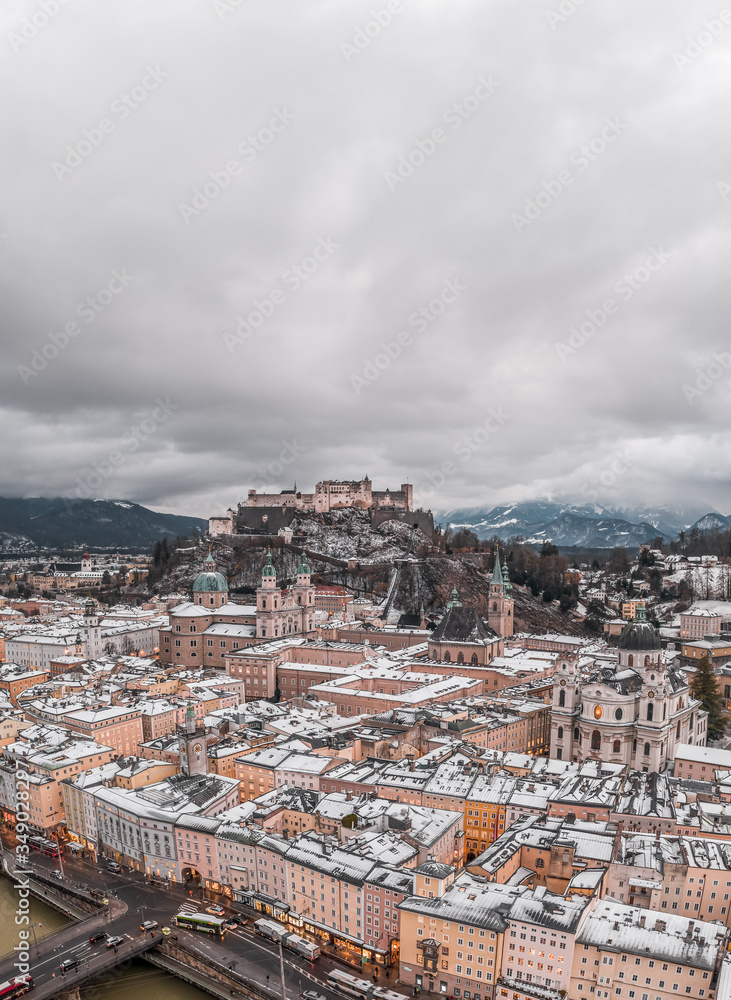 Aerial drone shot view of snowy Salzburg old town and Hohensalzburg fortress on the hill with heavy clouds in winter