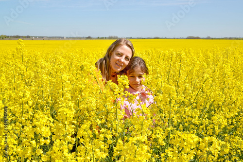 Young woman with daughter stand in flowering rapeseed field