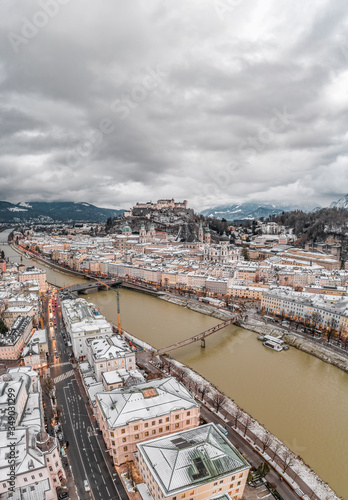 Aerial drone shot view of snowy Salzburg old town and Hohensalzburg fortress on the hill with heavy clouds in winter