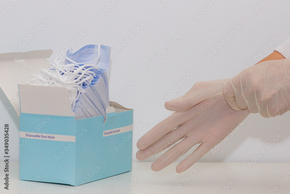 Women's hands putting on rubber gloves and a pack of face masks, white background