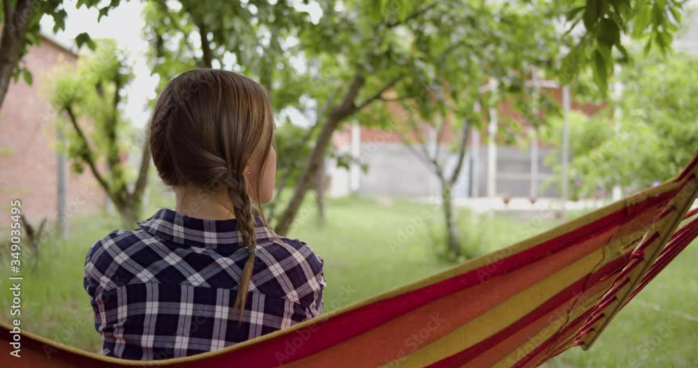 The girl is sitting back in the frame, swinging on a hammock