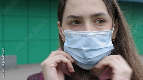 Caucasian girl puts a protective medical mask on her face on the street during a coronavirus epidemic in close-up