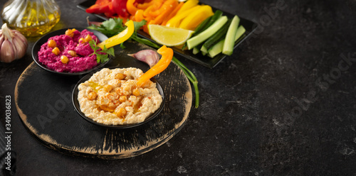 Variety of vegan hummus dips with colorful vegetable sticks on black background