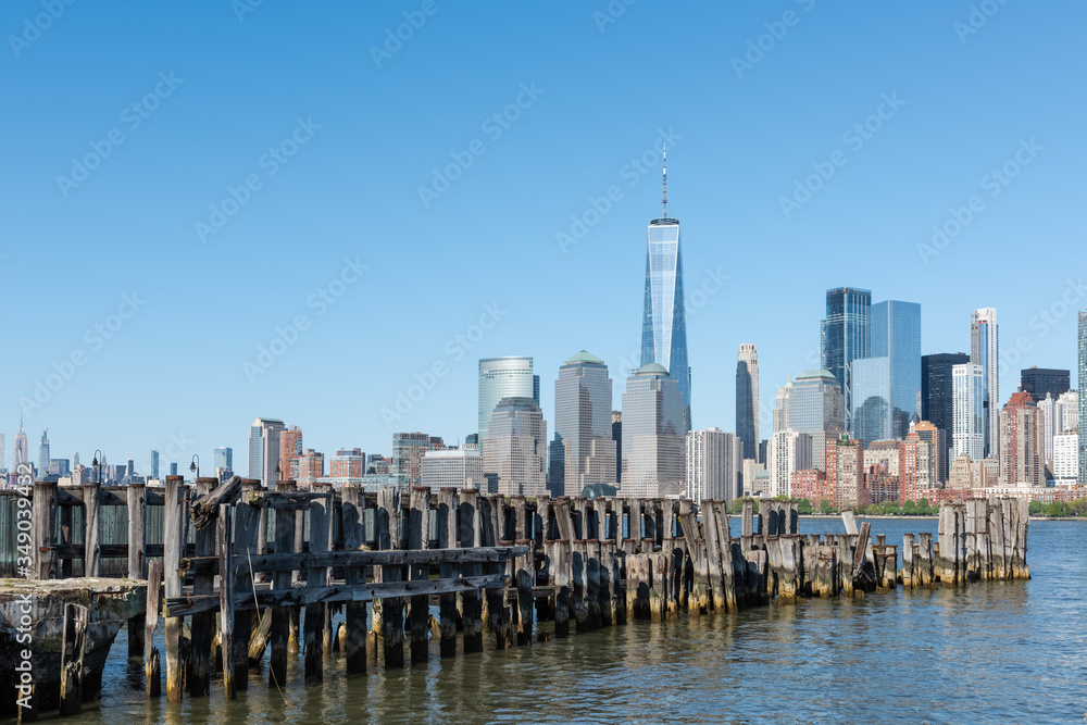 New York City Skyline with a dock and wooden pilings in the foreground on the Hudson River, on a summer day with a bright blue sky. 