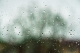 Window overlooking a rainy street. Gloomy evening weather with a view of the road. Drops on glass and bokeh from cars. Stock background for design