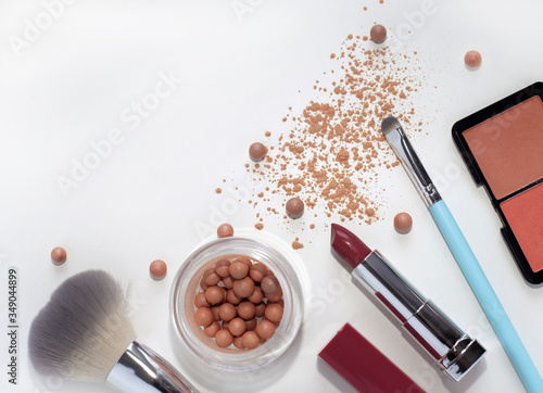 Bright decorative cosmetics: blush in balls, lipstick, cosmetic brushes, scattered powder on a white background.