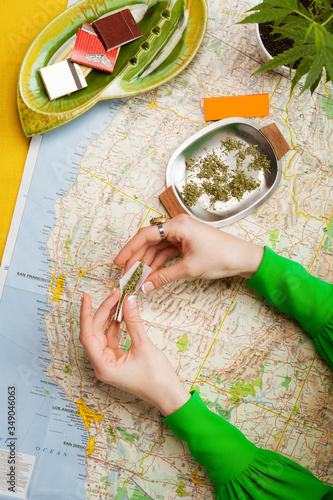 Hands in Green Sleeves Rolling Cannabis into Joints on Map of the West Coast (ID: 349046063)