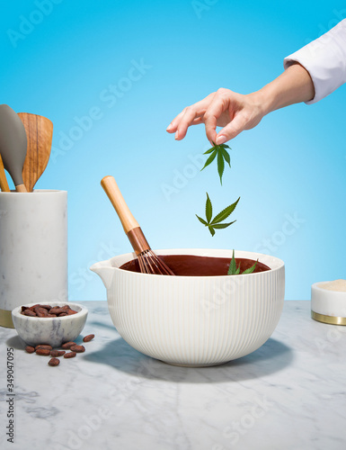 Chef Hand Adding Cannabis Leaves to Chocolate Mixing Bowl on Marble Countertop (ID: 349047095)