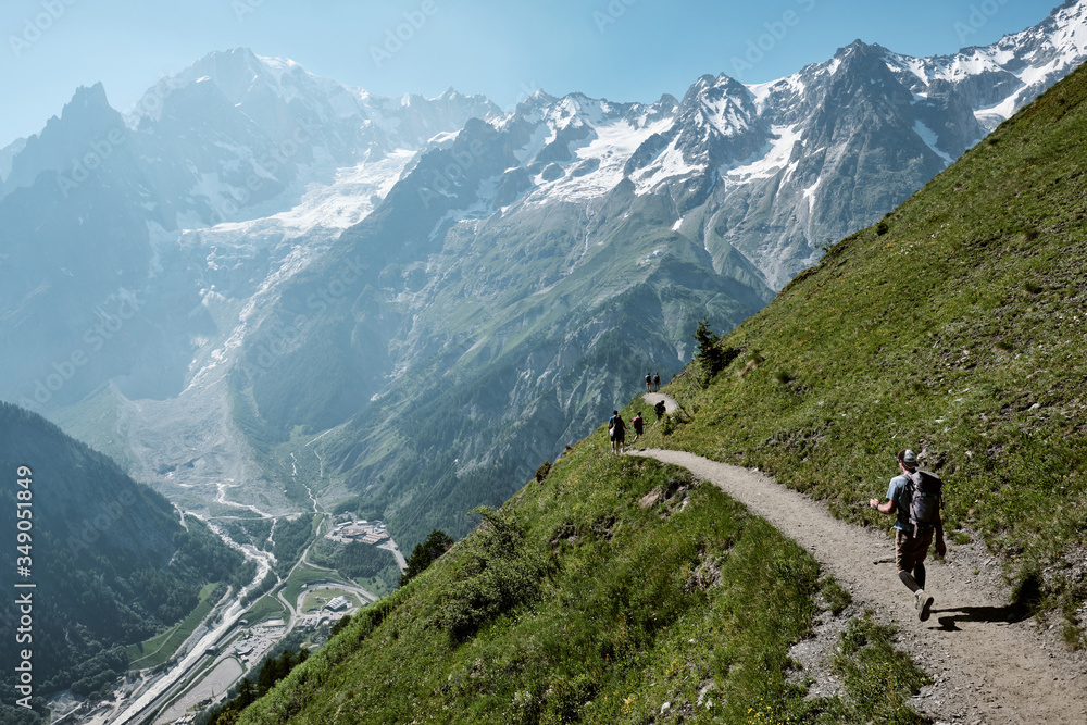 Man walking on a panoramic trail in the alps with Mont Blanc as a background in a sunny day