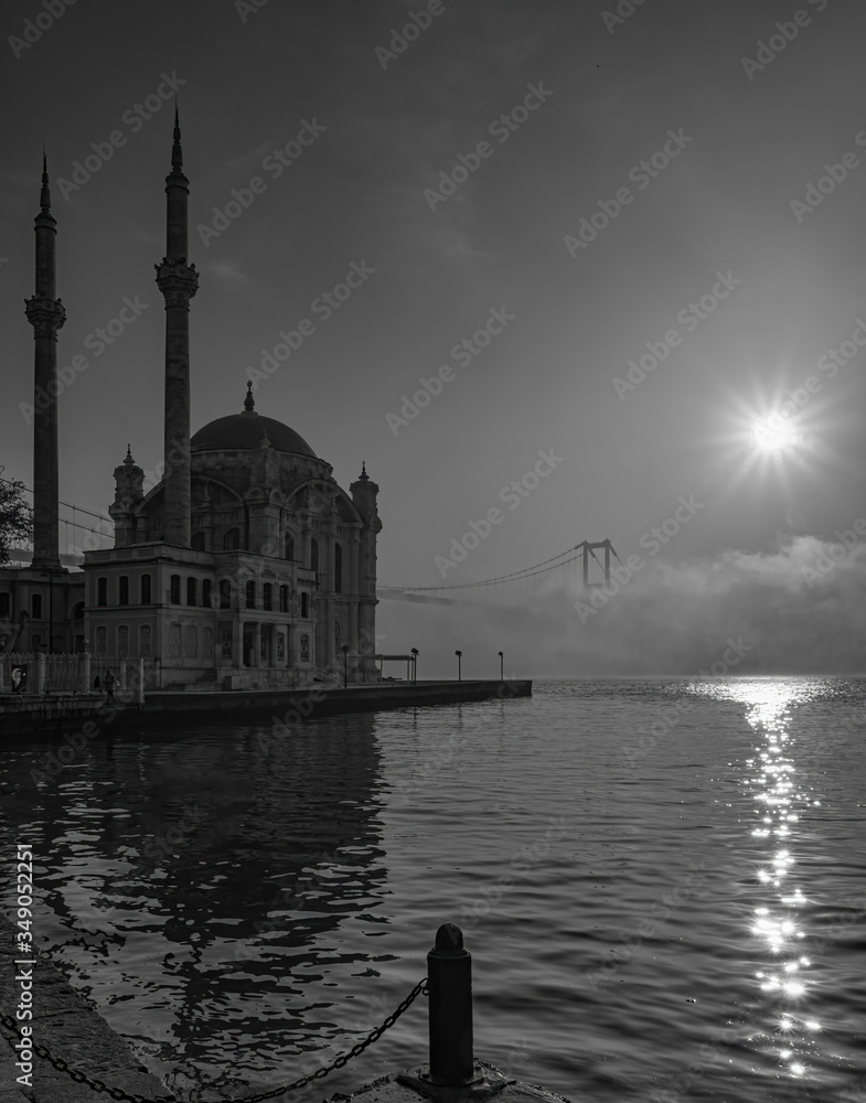 Naklejka premium Ortakoy Mosque and Bosphorus Bridge in Istanbul, Turkey. Dramatic sky. The 15 July Martyrs Bridge in a fog