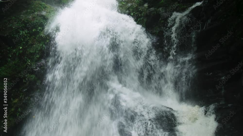 Tilt of dramatic waterfall gushing into a plunge pool below. The water is rushing very quickly down a granite mountain. There are rocks covered with green moss Tilt of dramatic waterfall gushing into a plunge pool below. The water is rushing very quickly down a granite mountain. There are rocks covered with green moss