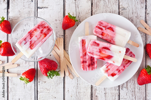 Homemade strawberry vanilla yogurt popsicles. Top view table scene on a rustic white wood background.