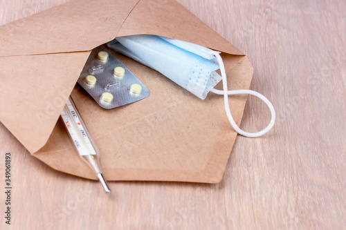 Parcel in craft envelope: mercury thermometer, pills and medical mask, on a wooden table