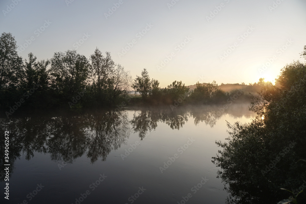 Beautiful morning river, a lake in light fog and the rays of the sun. Trees and bushes glow in the evening. Stock nature background for design.