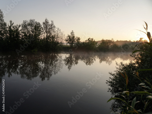 Beautiful morning river, a lake in light fog and the rays of the sun. Trees and bushes glow in the evening. Stock nature background for design.
