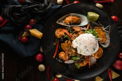 italian food background of black fettuccine spaghetti pasta with spiced seafood and poached egg in black palte on wooden table, selective focused