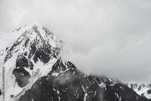 Atmospheric minimalist alpine landscape with massive hanging glacier on snowy mountain peak. Big balcony serac on glacial edge. Low clouds among snowbound mountains. Majestic scenery on high altitude.