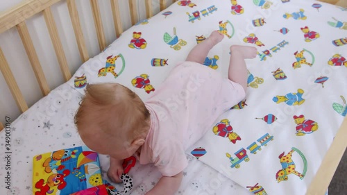 Baby lays on her tummy while pulling her foam toy book towards her inside of her cot photo