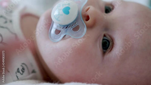 Close up adorable blue eyed baby sucks dummy as they wriggle on the floor photo