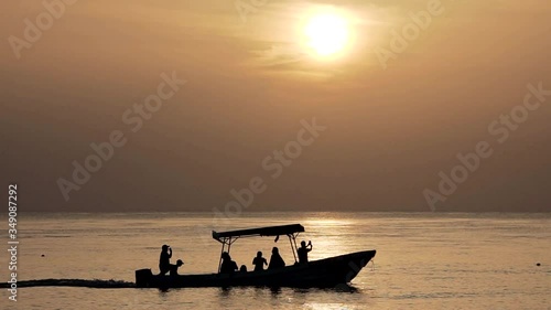 Boat in backlight and slow motion going from left to right while sun is falling at beach photo